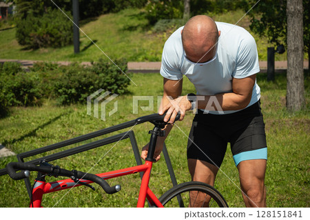 Man adjusting bicycle seat with hex key tool at nature public park. Summer activity. Man adjusting bicycle seat with hex key tool at nature public park. Summer activity. 128151841