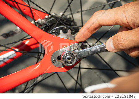 Close-up of person's hand using wrench to tighten component on red bicycle wheel, ensuring proper maintenance and optimal performance for cycling activities. Transmission repair. 128151842