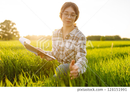 Young female farmer is studying with tablet young wheat in the field. Concept for farm development. Young female farmer is studying with tablet young wheat in the field. Concept for farm development. 128151991