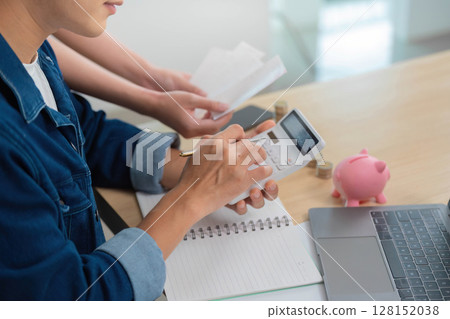 Calculating Finances. Young man using calculator for budgeting with piggy bank in view. Calculating Finances. Young man using calculator for budgeting with piggy bank in view. 128152038