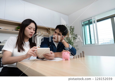 Couple Analyzing Finances. Young adults reviewing budget on tablet at home. 128152039