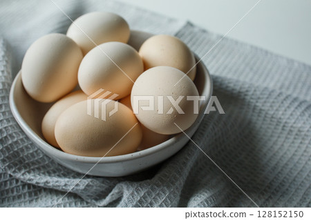 Fresh farm chicken eggs in bowl on grey kitchen towel close up Fresh farm chicken eggs in bowl on grey kitchen towel close up 128152150