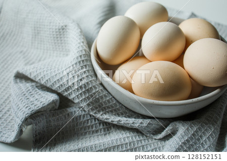 Fresh farm chicken eggs in bowl on grey kitchen towel close up Fresh farm chicken eggs in bowl on grey kitchen towel close up 128152151