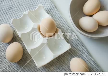 Chicken eggs in ceramic easter tray, kitchen bowl and on grey kitchen towel Chicken eggs in ceramic easter tray, kitchen bowl and on grey kitchen towel 128152155
