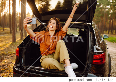 A woman in the trunk of a car at sunset. Traveling by car, camping. Active lifestyle. 128152188