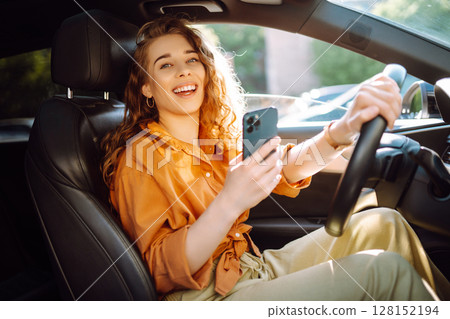 Happy woman in the car in the driver's seat looks at the smartphone. Business, technology concept. Happy woman in the car in the driver's seat looks at the smartphone. Business, technology concept. 128152194