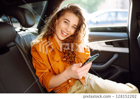 A young woman with a smartphone chats in the back seat of a car. Transport concept. Lifestyle. A young woman with a smartphone chats in the back seat of a car. Transport concept. Lifestyle. 128152202