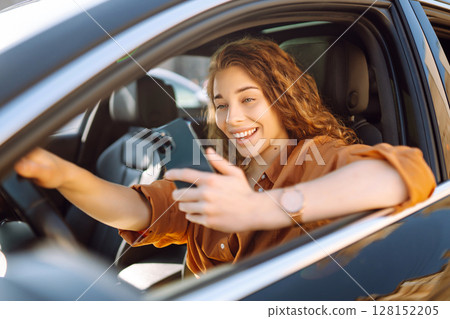 Happy woman in the car in the driver's seat looks at the smartphone. Business, technology concept. Happy woman in the car in the driver's seat looks at the smartphone. Business, technology concept. 128152205