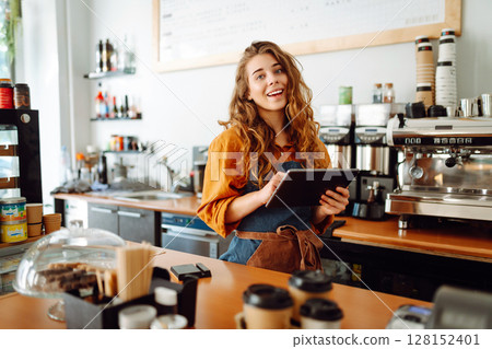 Beautiful woman owner stands behind the counter of a coffee shop. Business concept. Takeaway food. Beautiful woman owner stands behind the counter of a coffee shop. Business concept. Takeaway food. 128152401