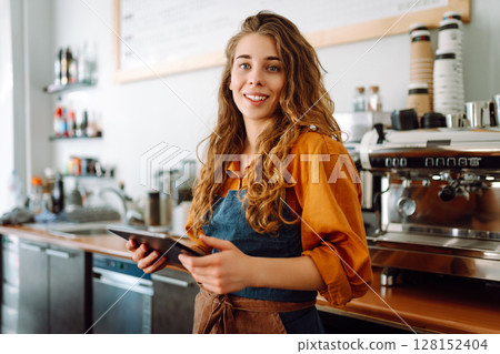 Beautiful woman owner stands behind the counter of a coffee shop. Business concept. Takeaway food. Beautiful woman owner stands behind the counter of a coffee shop. Business concept. Takeaway food. 128152404