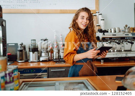 Beautiful woman owner stands behind the counter of a coffee shop. Business concept. Takeaway food. Beautiful woman owner stands behind the counter of a coffee shop. Business concept. Takeaway food. 128152405