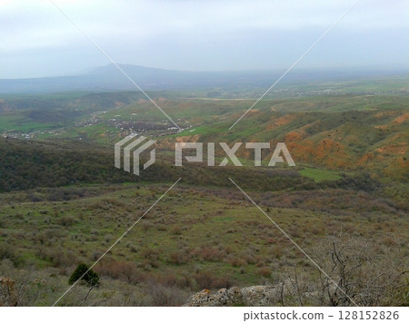 A sprawling valley with rolling green hills, a small village nestled in the distance, and faint mountains under a cloudy sky, capturing a peaceful rural landscape A sprawling valley with rolling green hills, a small village nestled in the distance, and faint mountains under a cloudy sky, capturing a peaceful rural landscape 128152826