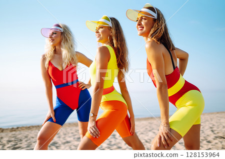 Dancing on beach. Woman in colorful swimsuits are dancing in morning. ?oncept of fitness, aerobics. 128153964
