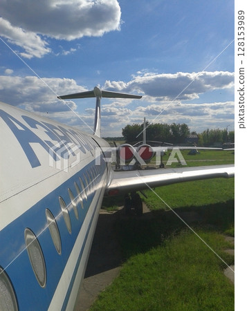 Side View of a Commercial Jet with Blue and White Design Parked in an Open Grassy Area Side View of a Commercial Jet with Blue and White Design Parked in an Open Grassy Area 128153989