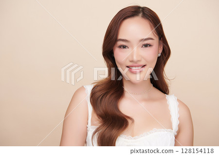 A beautiful young Asian woman with clean, fresh skin against a beige background. Skincare, facial treatment, cosmetology, beauty, and spa. An elegant portrait of an Asian woman. 128154118