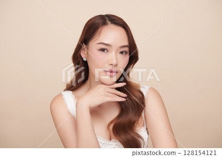 A beautiful young Asian woman with clean, fresh skin against a beige background. Skincare, facial treatment, cosmetology, beauty, and spa. An elegant portrait of an Asian woman. 128154121