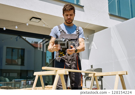 Carpenter working outside with electric jigsaw and small dog in backyard 128154224
