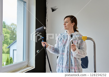 Woman holding paint roller and brush during painting wall at home Woman holding paint roller and brush during painting wall at home 128154232