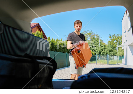 Man placing suitcase into car trunk before summer trip Man placing suitcase into car trunk before summer trip 128154237
