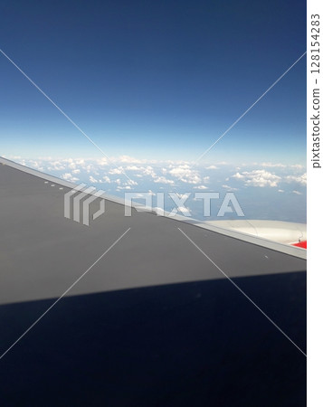 A breathtaking aerial view from an airplane window showcasing a vast expanse of fluffy white clouds against a deep blue sky, with the aircraft's wing prominently in the foreground A breathtaking aerial view from an airplane window showcasing a vast expanse of fluffy white clouds against a deep blue sky, with the aircraft's wing prominently in the foreground 128154283