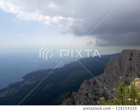 A dramatic view from a cliffside overlooking a lush green valley, a coastal town along the shoreline, and the vast blue sea under a partly cloudy and overcast sky A dramatic view from a cliffside overlooking a lush green valley, a coastal town along the shoreline, and the vast blue sea under a partly cloudy and overcast sky 128154310