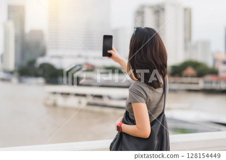 Happy solo southeast asian woman blogger and teenager take photo with smartphone. world travel explorer local cultural experience tourism concept Asia. Wait for express boat Chao Phraya river Happy solo southeast asian woman blogger and teenager take photo with smartphone. world travel explorer local cultural experience tourism concept Asia. Wait for express boat Chao Phraya river 128154449