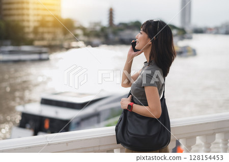 Content solo southeast asian woman teenager blogger on travel tourism in Bangkok Thailand. An explorer wait for local boat on Chao Phraya river in Asia using smartphone Content solo southeast asian woman teenager blogger on travel tourism in Bangkok Thailand. An explorer wait for local boat on Chao Phraya river in Asia using smartphone 128154453