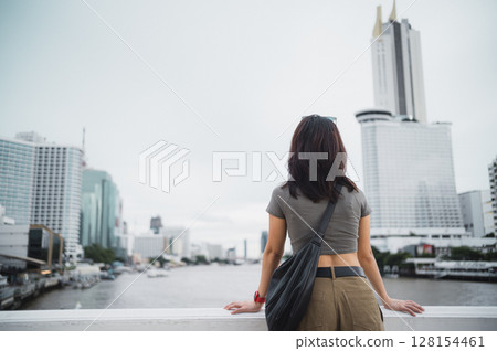 Solo Southeast Asian woman teenager blogger and world travel explorer local cultural experience. Wait for boat to express unique tourism concept Chao Phraya river Bangkok Thailand, Asia 128154461