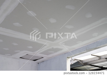 Interior renovation progress building smooth gypsum board ceiling edges. Plastering complete on ceilings showing precise work. Electrical wire visible reflecting effort towards finishing Interior renovation progress building smooth gypsum board ceiling edges. Plastering complete on ceilings showing precise work. Electrical wire visible reflecting effort towards finishing 128154471