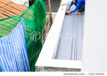 Diligent construction worker installs corrugated metal sheet roof panel using pu foam for insulation and sealing. Manual labor building rooftop demonstrates hard work and focus while working with Diligent construction worker installs corrugated metal sheet roof panel using pu foam for insulation and sealing. Manual labor building rooftop demonstrates hard work and focus while working with 128154484
