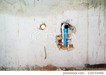 Damaged concrete wall with an exposed blue pipe in hole during major house renovation. Plumbing system work part of construction project with messy background view 128154488