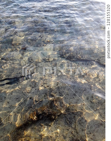 A serene and captivating view of clear water gently rippling over a textured, rocky surface beneath the sunlight's warm embrace A serene and captivating view of clear water gently rippling over a textured, rocky surface beneath the sunlight's warm embrace 128155320