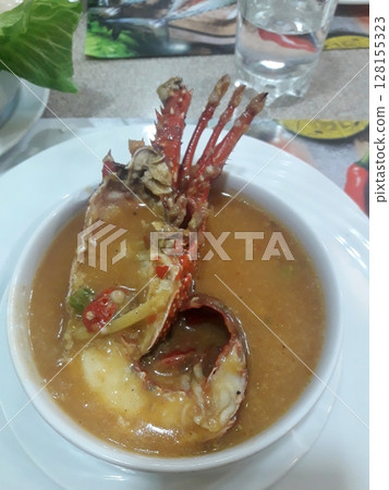Delicious lobster dish served in a rich, flavorful broth with vegetables and garnished with fresh herbs on a white plate 128155323