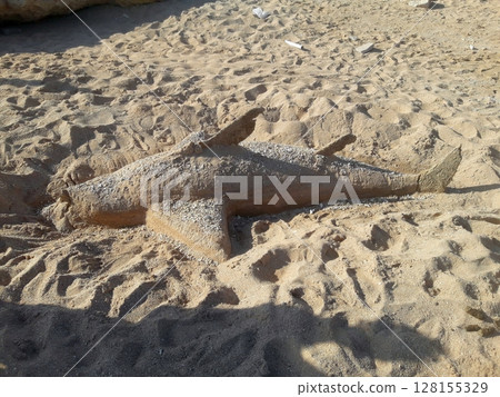 A detailed sand sculpture of a fish, intricately carved and lying on the beach, showcasing the artistry and creativity of sand sculpting 128155329