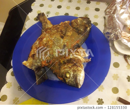 A freshly grilled whole fish served on a blue plate, with golden brown skin and crispy edges, ready to be enjoyed as a delicious meal 128155330