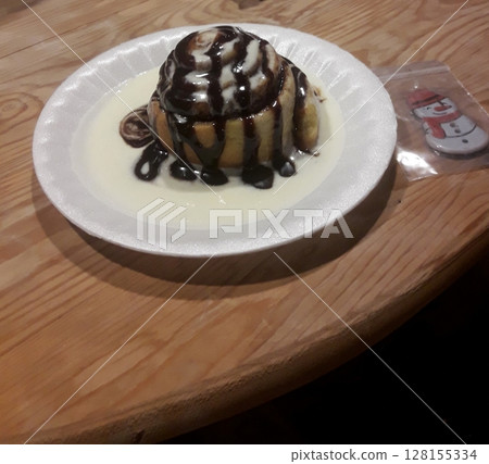 A delicious dessert served on a white plate, featuring a pastry drizzled with chocolate sauce and placed on a wooden table with a festive snowman decoration nearby 128155334