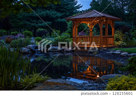 Illuminated Gazebo Reflecting in Serene Garden Pond at Dusk. Illuminated Gazebo Reflecting in Serene Garden Pond at Dusk. 128155601