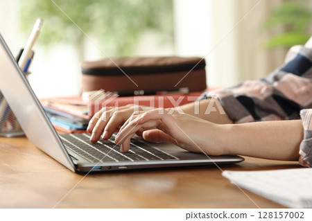 Student hands typing on laptop on a wooden table 128157002