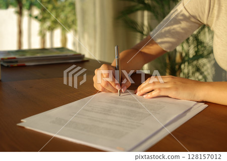 Woman hand signing document on a wooden table at home Woman hand signing document on a wooden table at home 128157012