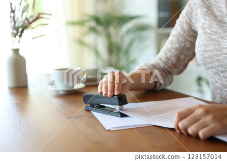Woman hand stapling papers on a wooden table at home Woman hand stapling papers on a wooden table at home 128157014