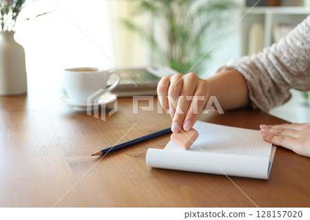 Woman hand using rubber erasing text on a wooden table at home 128157020