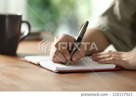 Woman hand writing on paper agenda on wooden table Woman hand writing on paper agenda on wooden table 128157021