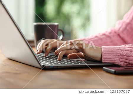 Woman hands writing on laptop on a wooden table Woman hands writing on laptop on a wooden table 128157037