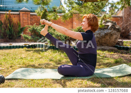 Woman doing a stretching exercise with a wooden stick during outdoor mobility practice. Posture alignment, shoulder opening, and spine flexibility. Woman doing a stretching exercise with a wooden stick during outdoor mobility practice. Posture alignment, shoulder opening, and spine flexibility. 128157088