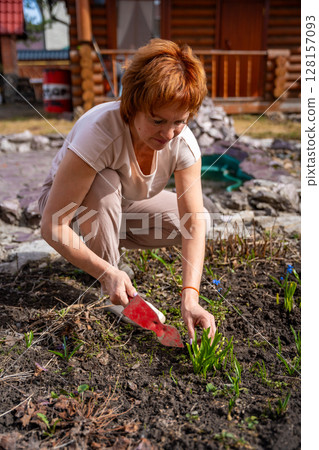 Woman planting flowers in her backyard garden during a quiet day at home. Gardening, nature connection, and mindful outdoor lifestyle. 128157093