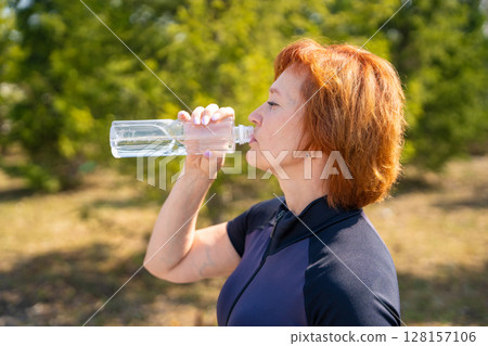 Woman drinking water during a short break in outdoor workout. Hydration, recovery, and healthy exercise routine. 128157106