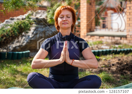 Woman meditating outdoors in a peaceful park setting during her morning routine. Mindfulness, mental balance, and emotional self-care. 128157107