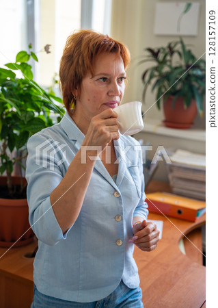 Woman taking a coffee break at her desk in a quiet office setting. Mindful pause, mental reset, and slow work lifestyle. 128157109