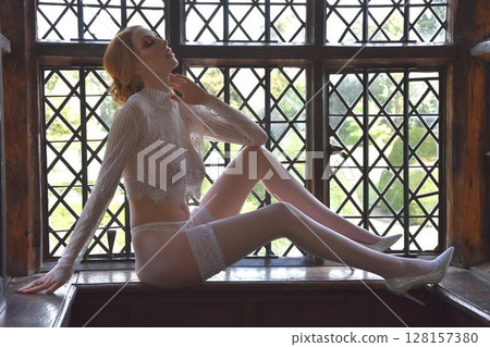 Beautiful, redheaded girl dressed in lace, posing in rooms of an old Manor House 128157380