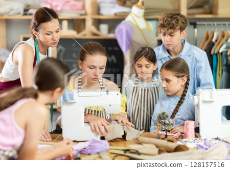 Teen girl sewing at machine in classroom with teacher support 128157516